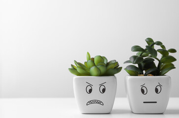 Beautiful potted houseplants with angry and concerned faces on white table, space for text....