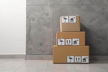 Many closed cardboard boxes with packaging symbols on floor indoors, space for text. Delivery service