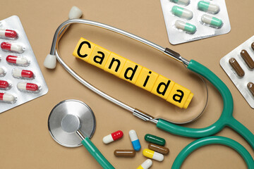 Yellow cubes with word Candida, stethoscope and pills on light brown background, flat lay