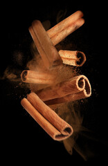 Aromatic cinnamon sticks and powder flying on black background