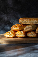 Sausage rolls, freshly baked and cooling on a wooden chopping board. On a Black stone background