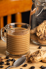 Top view of glass of latte on wooden table with spoon, coffee beans, cookies, chair and black background, selective focus, vertical