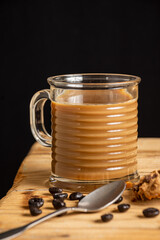 Close-up of glass of latte on wooden table with spoon and coffee beans, black background, selective focus, vertical