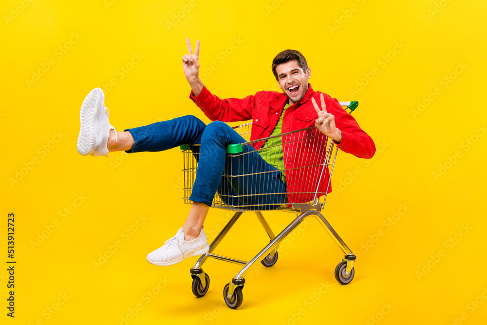 Poster full length body size view of attractive cheerful childish guy riding cart showing v-sign isolated o