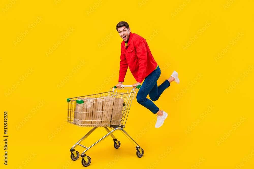 Poster full length body size view of attractive funny cheerful guy holding cart jumping isolated over brigh