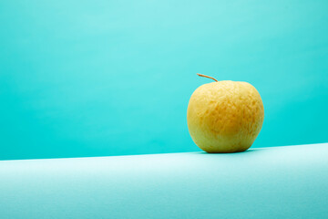 Old, not fresh apple on blue background.