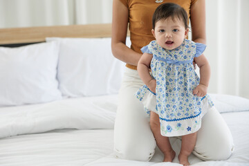 Fototapeta premium baby girl learning to walk and mother or sitter support her on bedroom