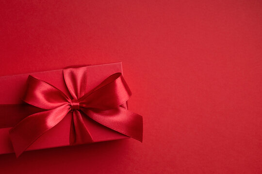 Red gift box with red bow on red background for Christmas or Valentine's day.