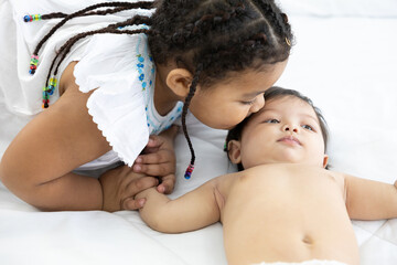 African kid kissing infant baby on bedroom