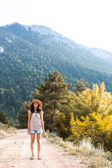 Naklejka premium A girl with a backpack and a straw hat walks along a mountain path