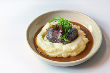 Traditional ox cheeks on potato puree with brown red wine sauce and garnish from wild herb leaves in a rustic bowl on a light table, copy space, selected focus