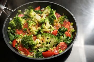 Vegetable pan with broccoli, tomatoes, spring onions and spinach on the stove, cooking healthy vegetarian food from fresh ingredients, selected focus