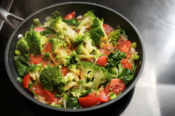 Vegetable pan with broccoli, tomatoes, spring onions and spinach on the stove, cooking healthy...