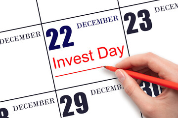 Hand drawing red line and writing the text Invest Day on calendar date December 22. Business and financial concept.