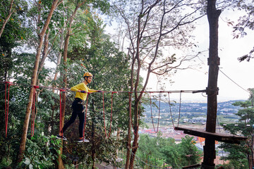 Young woman with climbing gear in an adventure extreme park climbing or passing on the rope road.