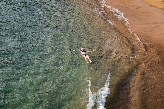 top view of woman floating in the sea near sandy beach