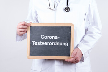 Arzt hält eine Tafel auf der Corona Testverordnung steht