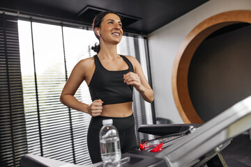 Fototapeta na wymiar Happy young caucasian woman in good mood on treadmill. Brunette wears sports top and leggings. Strength exercise concept