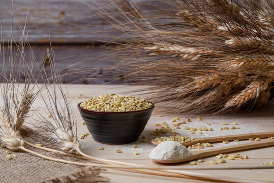 Bowl full of tender wheat seeds and dried ears of wheat along with a tablespoon of wheat flour. Different stages of wheat