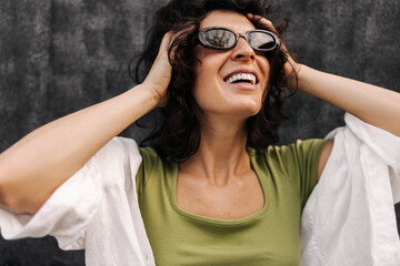 Close-up of joyful young caucasian brunette woman looking away holding her head. Girl with bob haircut wears sunglasses. Emotion concept