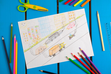 Child draws a pencil drawing of the city, cars and air pollution. Top view.