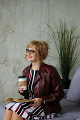 Business girl in the interior sitting drinking tea in a paper cup. Woman with glasses holding takeaway coffee to go.