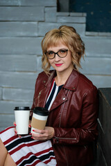 Business girl in the interior sitting drinking tea in a paper cup. Woman with glasses holding takeaway coffee to go.