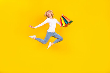 Fototapeta na wymiar Full body photo of nice young blond lady jump with bags wear shirt jeans footwear isolated on yellow background