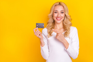 Photo of funny shiny young woman wear white shirt pointing bank card empty space isolated yellow color background