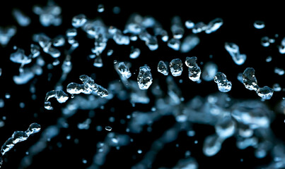 Drops of water splash blue water on a black background, concept of freshness drink, watering the rain source of pure water fountain copy space