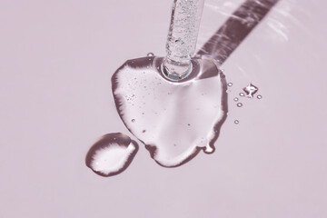 A cosmetic product gel or collagen serum flows out of a pipette with bubbles on pink background.