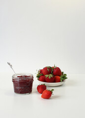 Homemade strawberry preserves or jam in a mason jar surrounded by fresh organic strawberries. Selective focus.