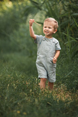 a blond boy in a gray t-shirt and gray overalls walks in the park
