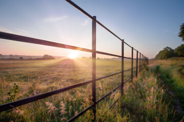 Sunrise through metal fence in rural landscape