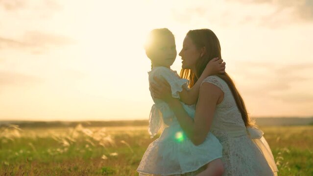 Carefree childhood, joyful girl smiling, hugging mother and kid. Child, daughter hugs her mother in summer park in sun. Happy family on walk in field in nature. Parent, kid play together at sunset