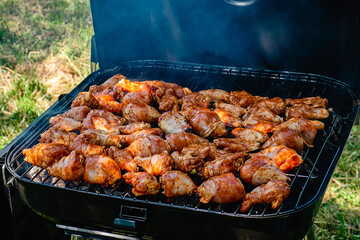 Spicy chicken legs and wings grilling in a portable barbecue.