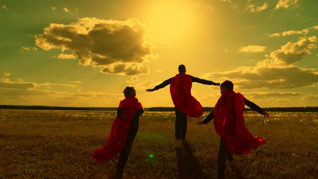 Little hero in red cloak running into sunset. Happy children run, play superheroes against sky. Boys play red cape superhero, childhood dream. Victorious child in raincoat plays Children dream, nature