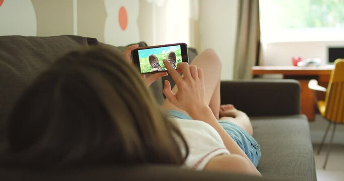 A woman looking through photos on her cellphone while relaxing on her couch