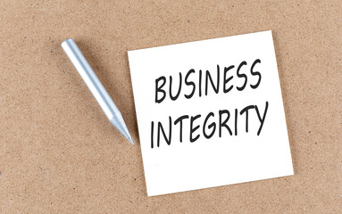 BUSINESS INTEGRITY text on sticky note on a cork board with pencil ,