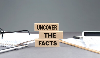 UNCOVER THE FACTS text on wooden block with notebook,chart and calculator, grey background