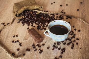 Roasted coffee beans in little bag with ropes and cup of coffee with drink and chocolate on brown...