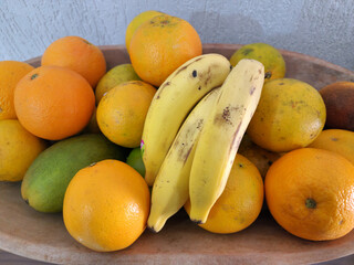 rustic fruit bowl with oranges, banana and mango on the wooden table