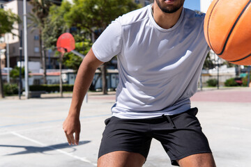 Fototapeta premium Close up view of an unrecognizable young muslim man playing basketball in the street, city life and training and sport concept