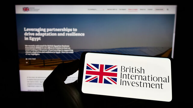 Stuttgart, Germany - 06-25-2022: Person holding cellphone with logo of British International Investment (BII) on screen in front of business webpage. Focus on phone display.