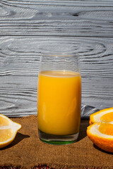 A composition of fresh fruit and drink. Orange lying and lemon around an orange juice in a glass, on a dark textured wooden table covered with a cloth.