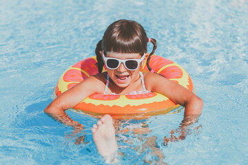 close-up portrait of a toddler girl 4 years old swims in the pool in the summer in an inflatable circle, vacation concept