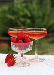 Spritz cocktails and fresh strawberry in a glass bowl. Picnic in the garden. Glass tableware close up photo. Rustic still life with seasonal fruit. 