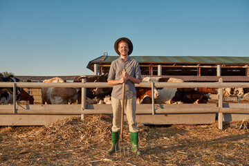 Smiling male farmer near paddock with cows on farm