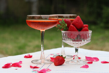 Glass with cocktail and fresh strawberry on a garden table. Green tree leaves on a background. Summer day evening. 