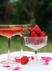 Spritz cocktails and fresh strawberry in a glass bowl. Picnic in the garden. Glass tableware close up photo. Rustic still life with seasonal fruit. 